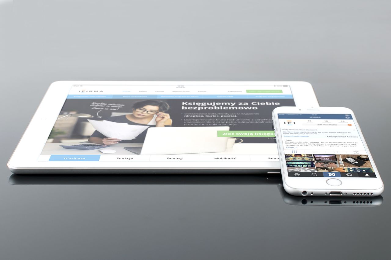 Tablet y smartphone modernos mostrando contenido web sobre una superficie reflectante, destacando la tecnología y la conectividad.